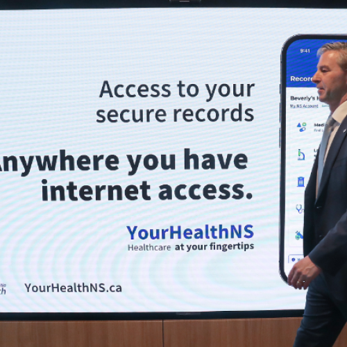 premier houston walks by a a screen with health records information on it. 